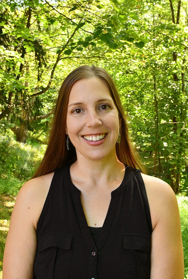 A woman with brown hair wearing a black shirt smiles at the camera.