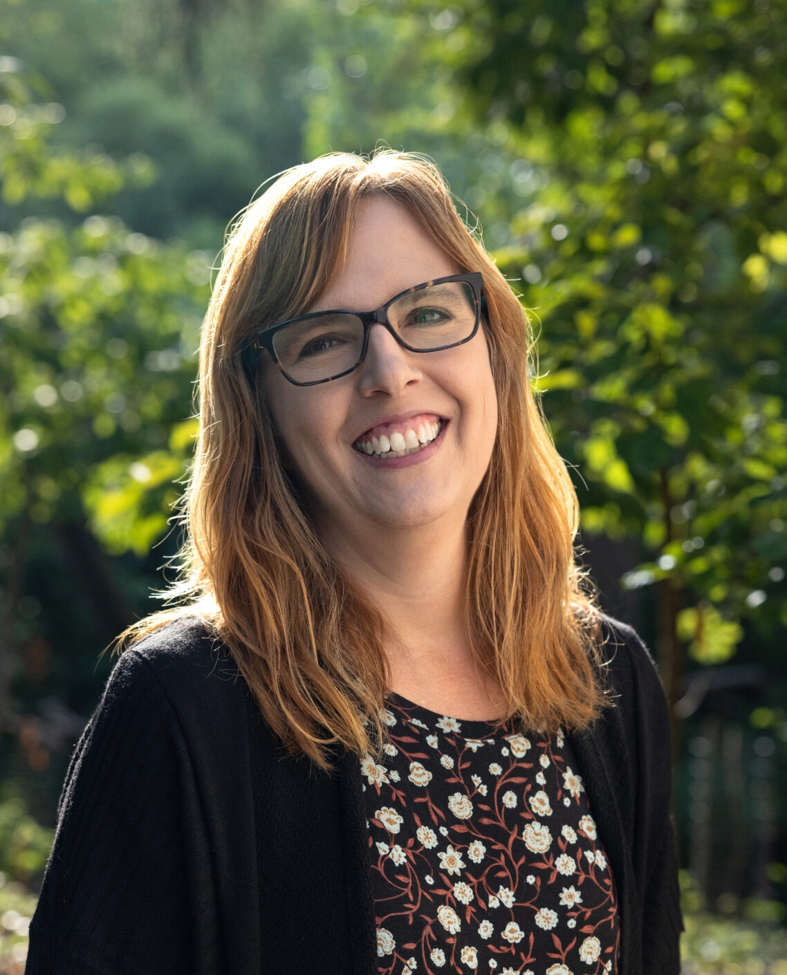 A woman with a floral top and dark blond hair smiles at the camera