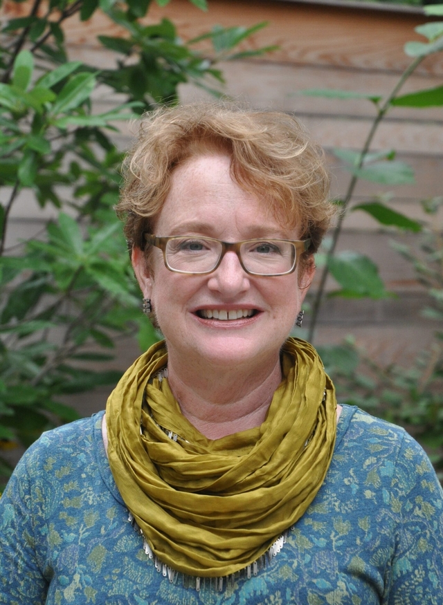 A woman with short hair with yellow scarf around her neck smiles at the camera.