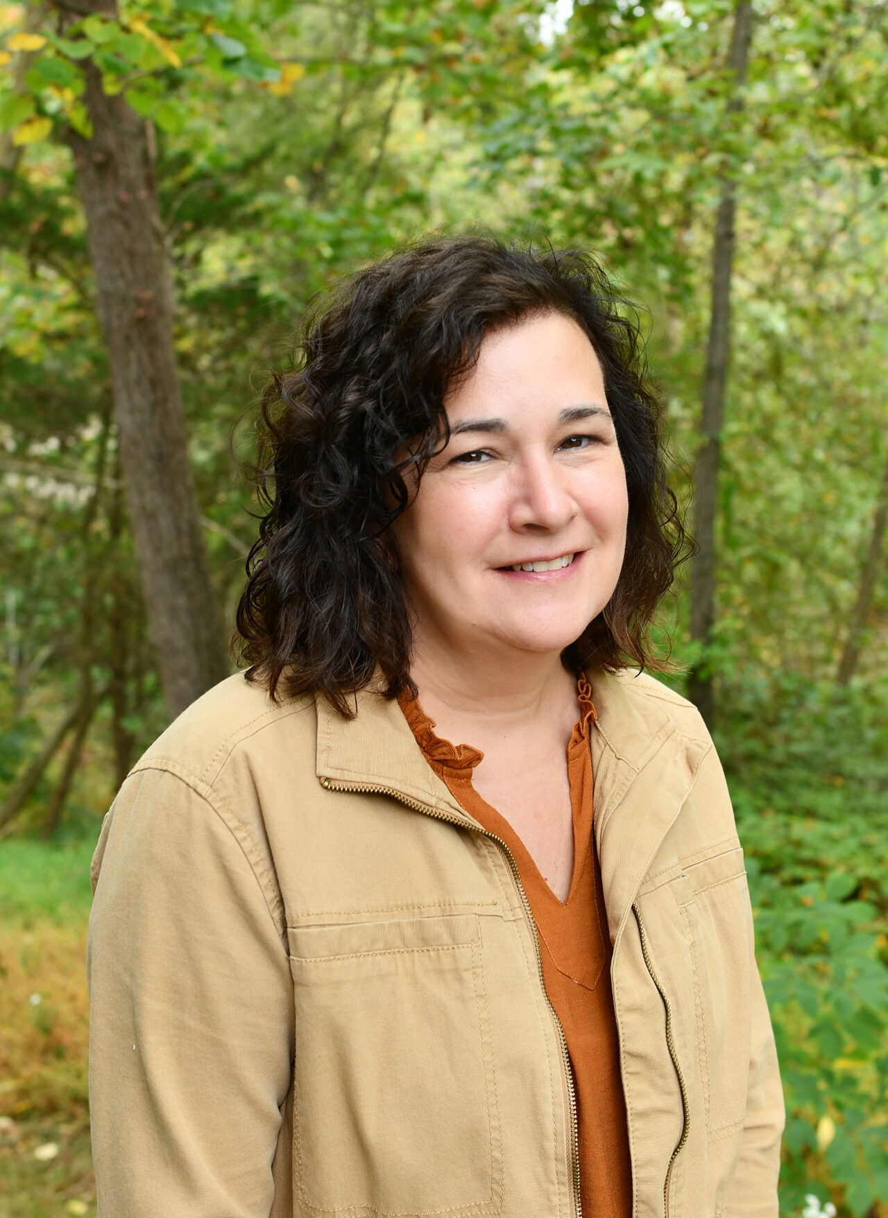 A woman with dark hair and a beige jacket smiles at the camera.