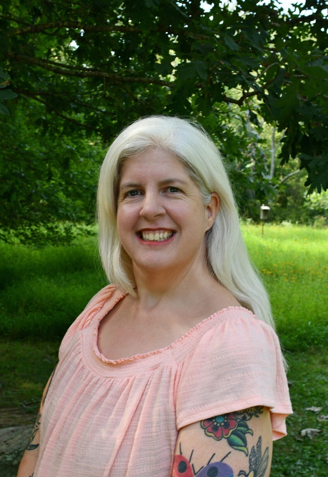 A woman with long white hair and a pink shirt smile at the camera.