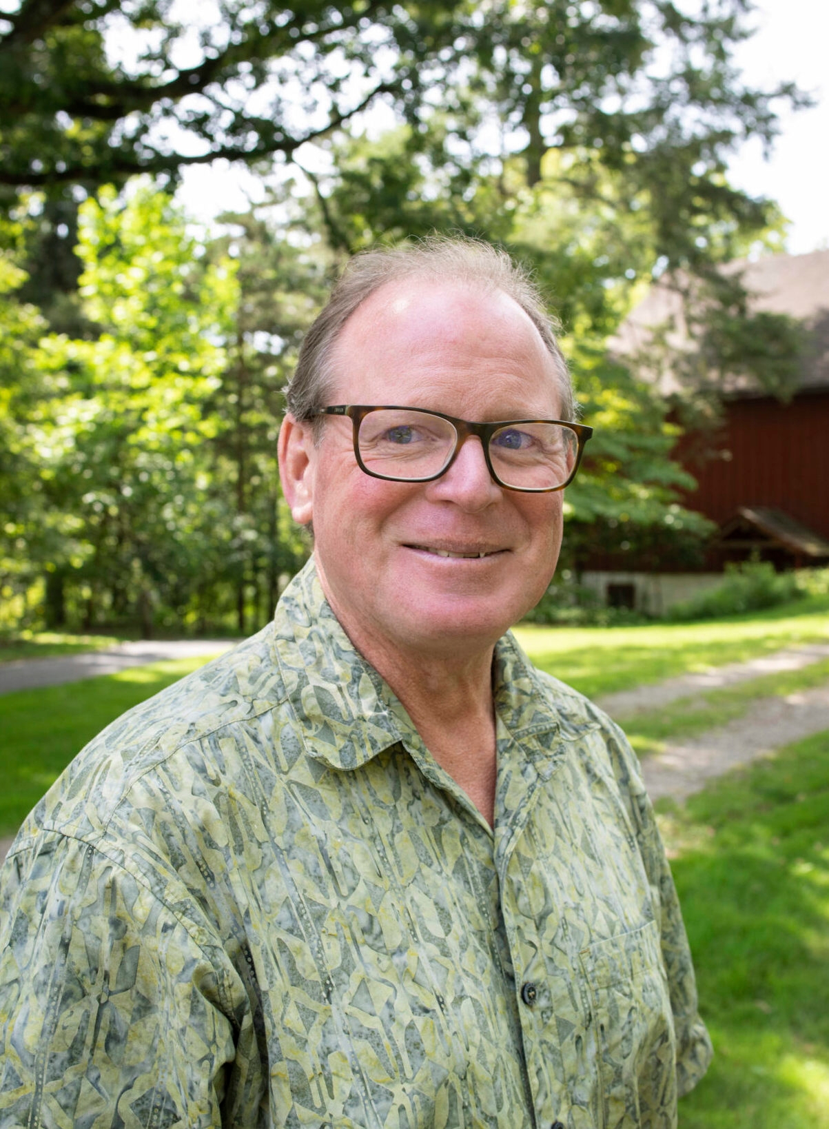 A man in glasses and a printed green shirt smiles at the camera.