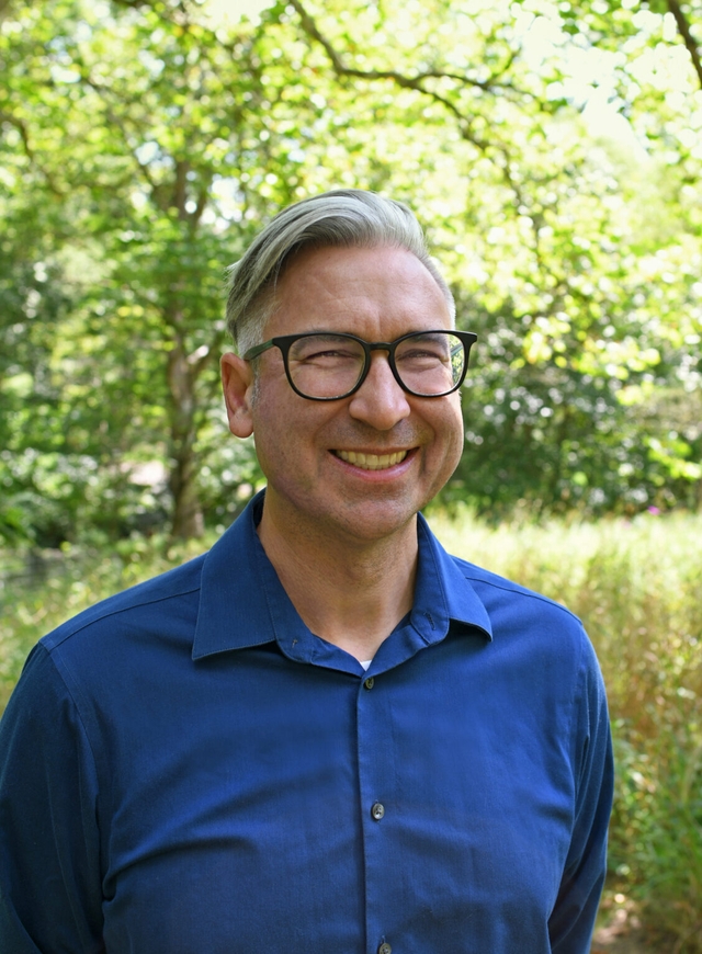 A man in glasses and a blue shirt smiles at the camera