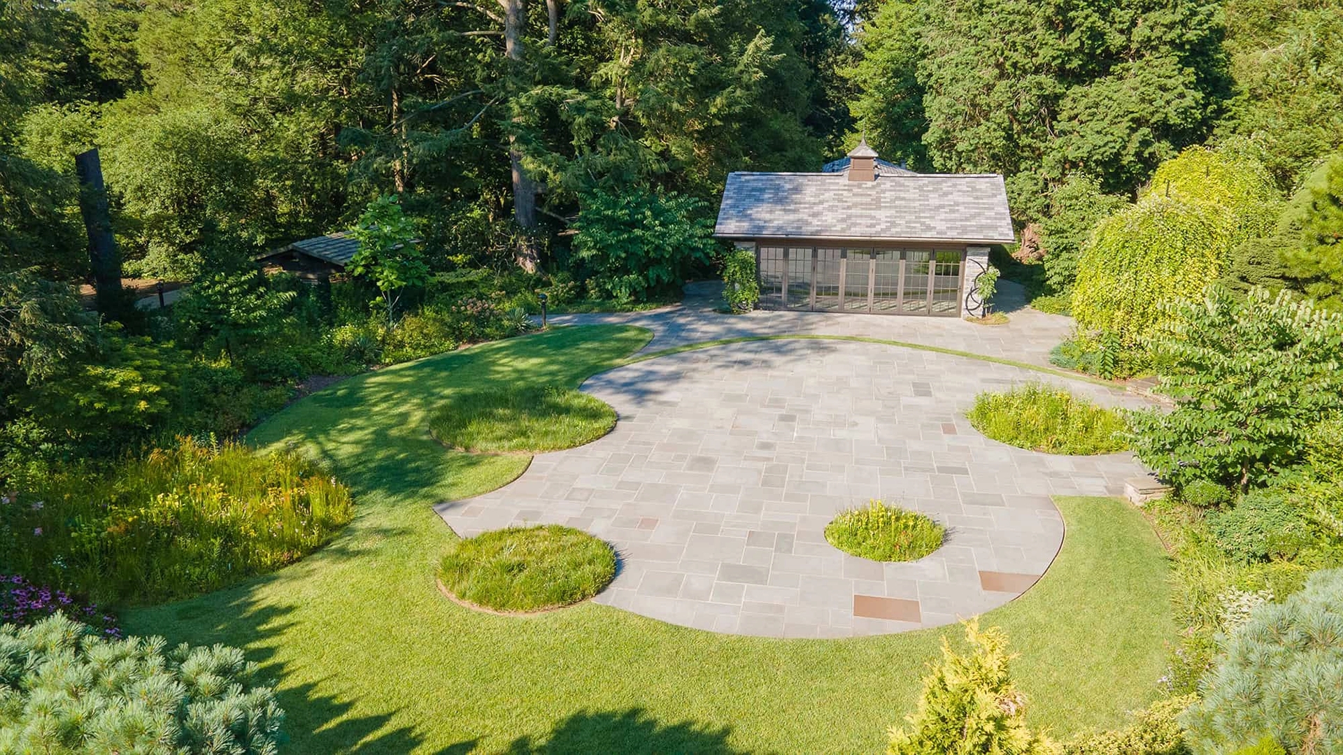 Photo by Benjamin Szmidt
 - A drone photo of the Pool House at Stoneleigh surrounded by bluestone pavers with circular bog gardens.
