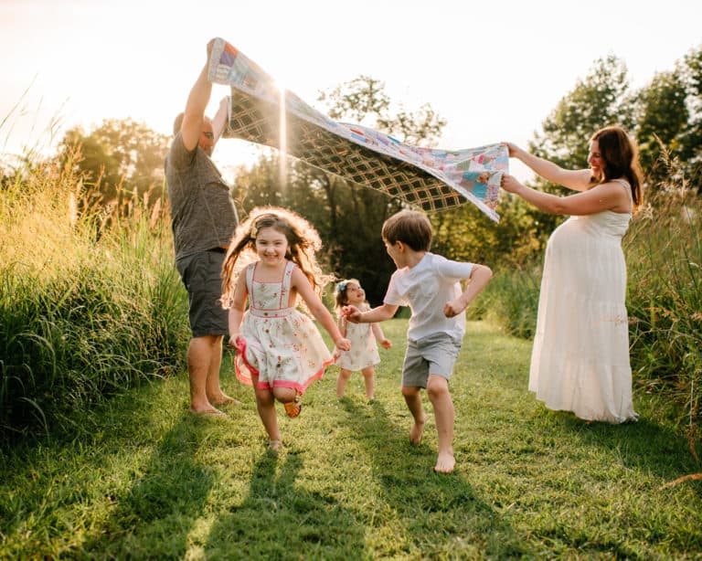 Three children run in the sunshine with their parents at a nature preserve