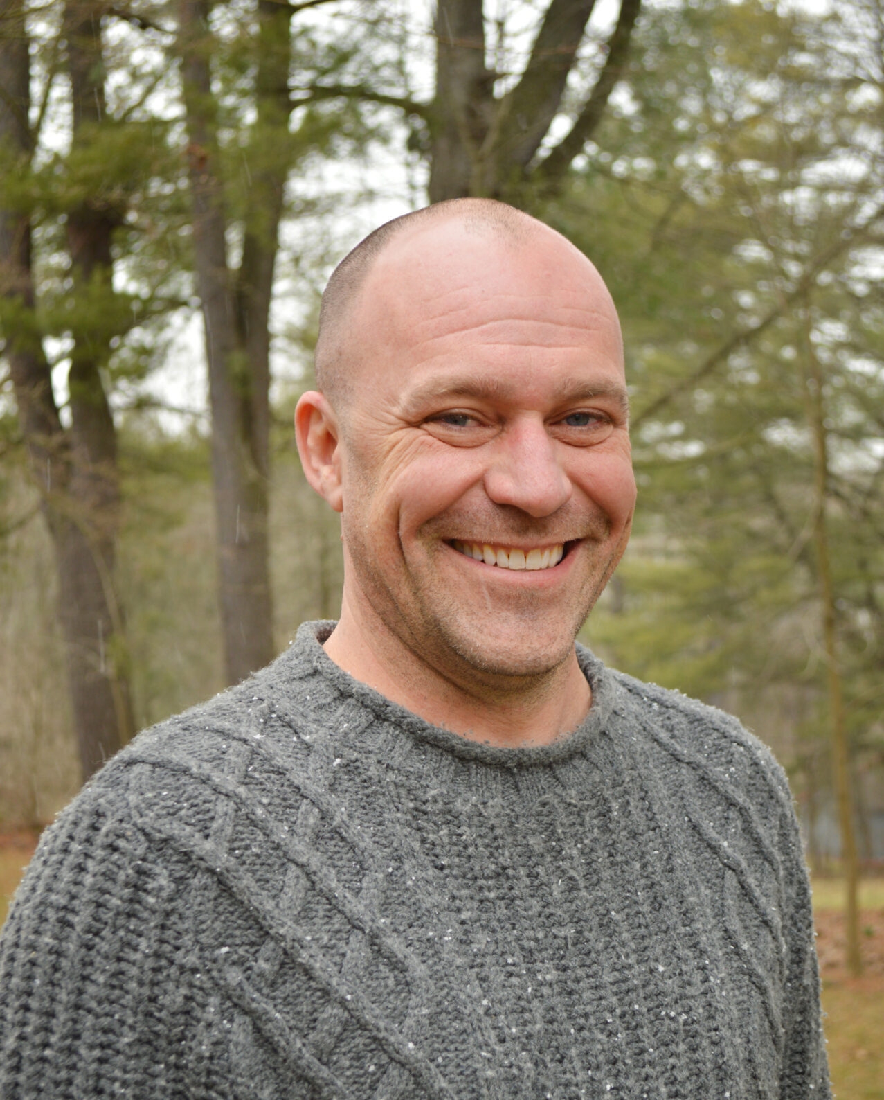 a bald, smiling man wearing a gray sweater