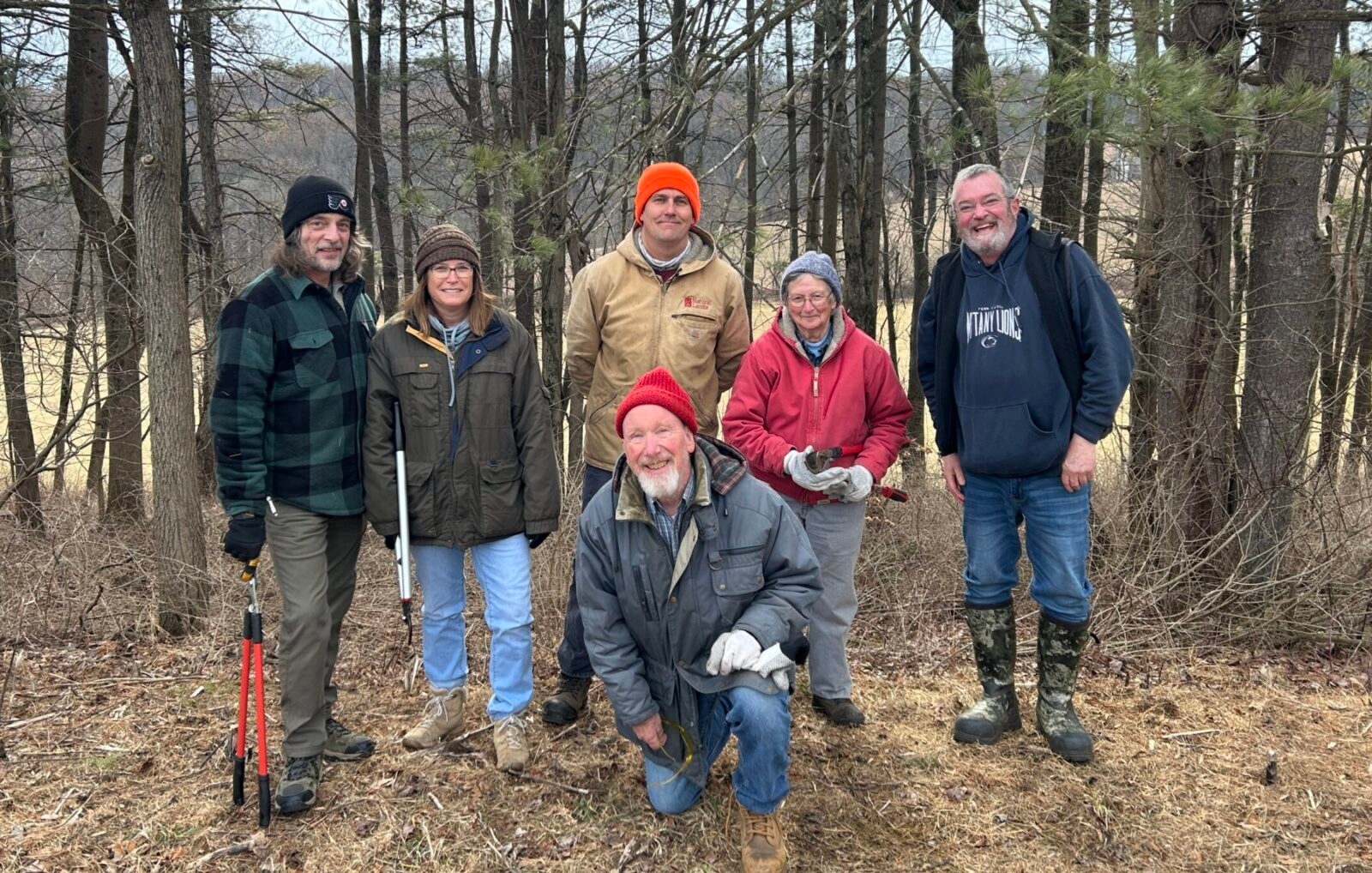 Volunteers posing in front of the woods they are taking care of.