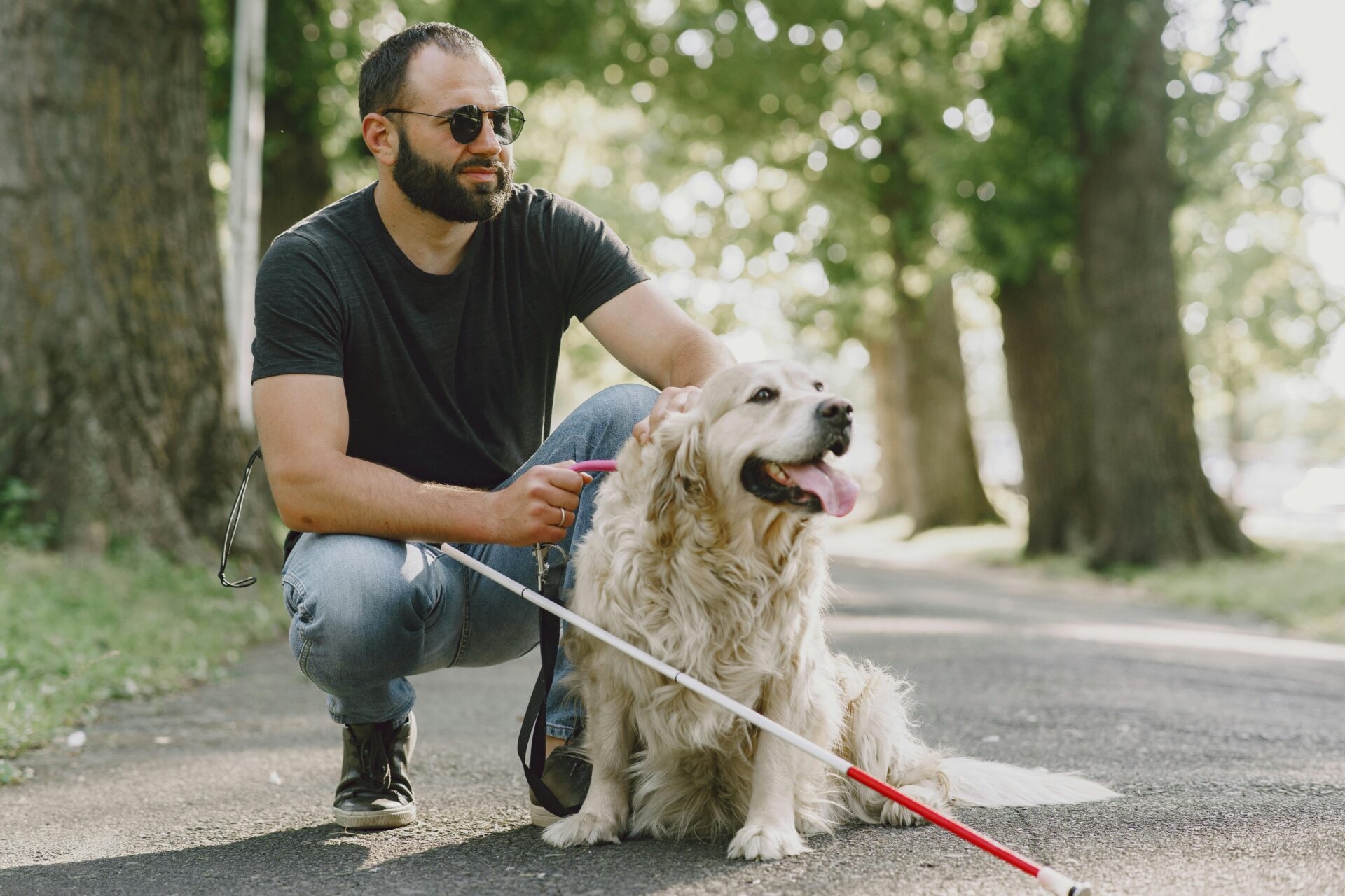 a man with a mobility aid in a black crew neck t-shirt and blue denim jeans holding a white dog