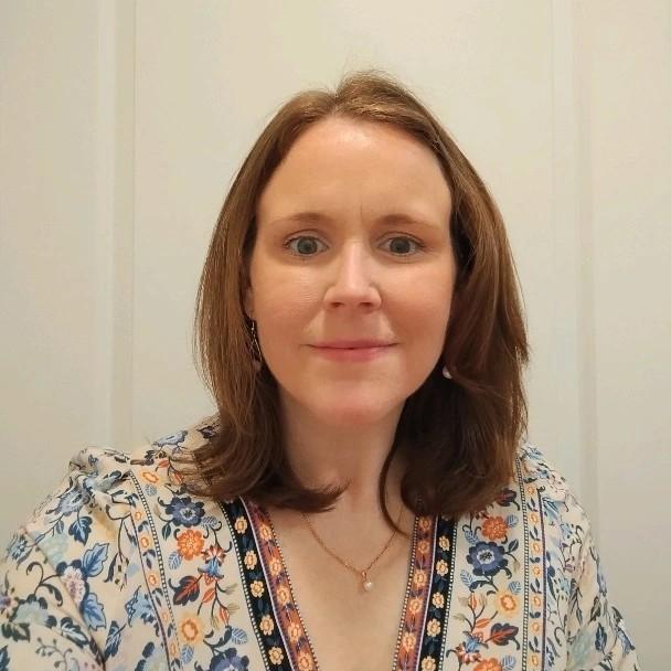 A photo of a woman with shoulder-length hair in a floral top smiles at the camera.