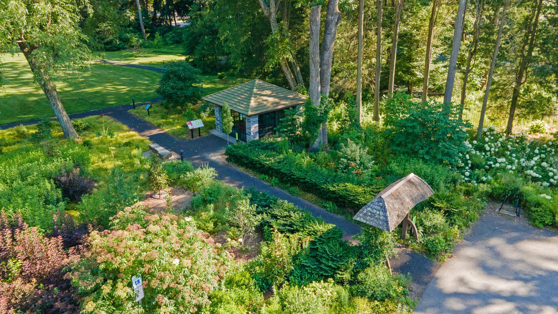 an aerial view of a garden with an arch structure, a square building, and a paved path