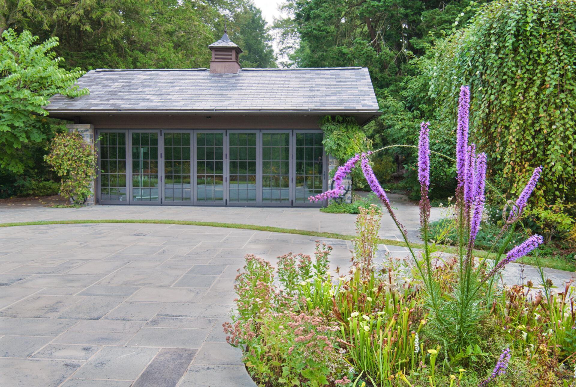 a circular garden bed surrounded by a patio with a rectangular building that has floor to ceiling windows