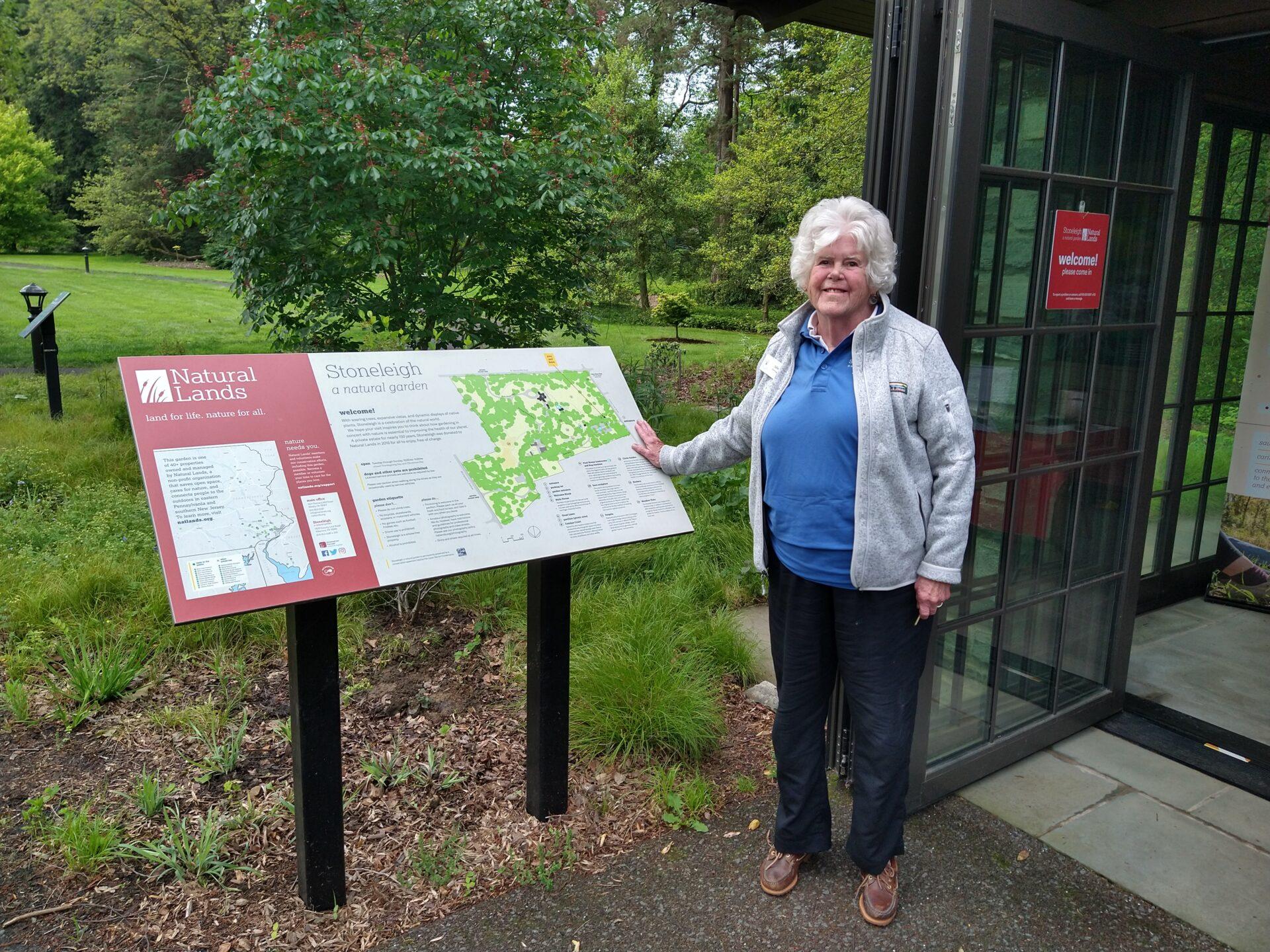 a woman in a blue shirt and fleece jacket standing in front of a sign with a map