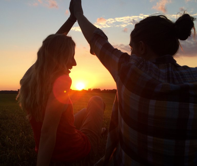 Two people high five in outdoors while the sun sets in the background.