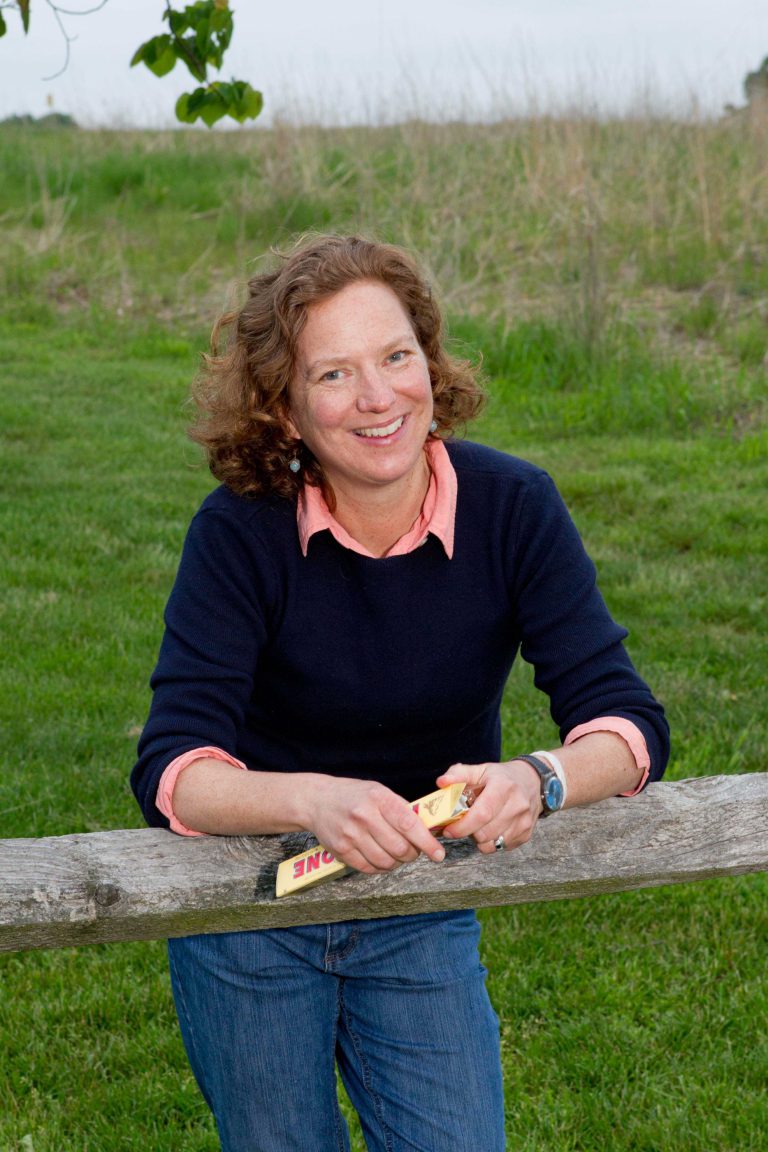 Suzanne Barton leans on a wooden fence outdoors.