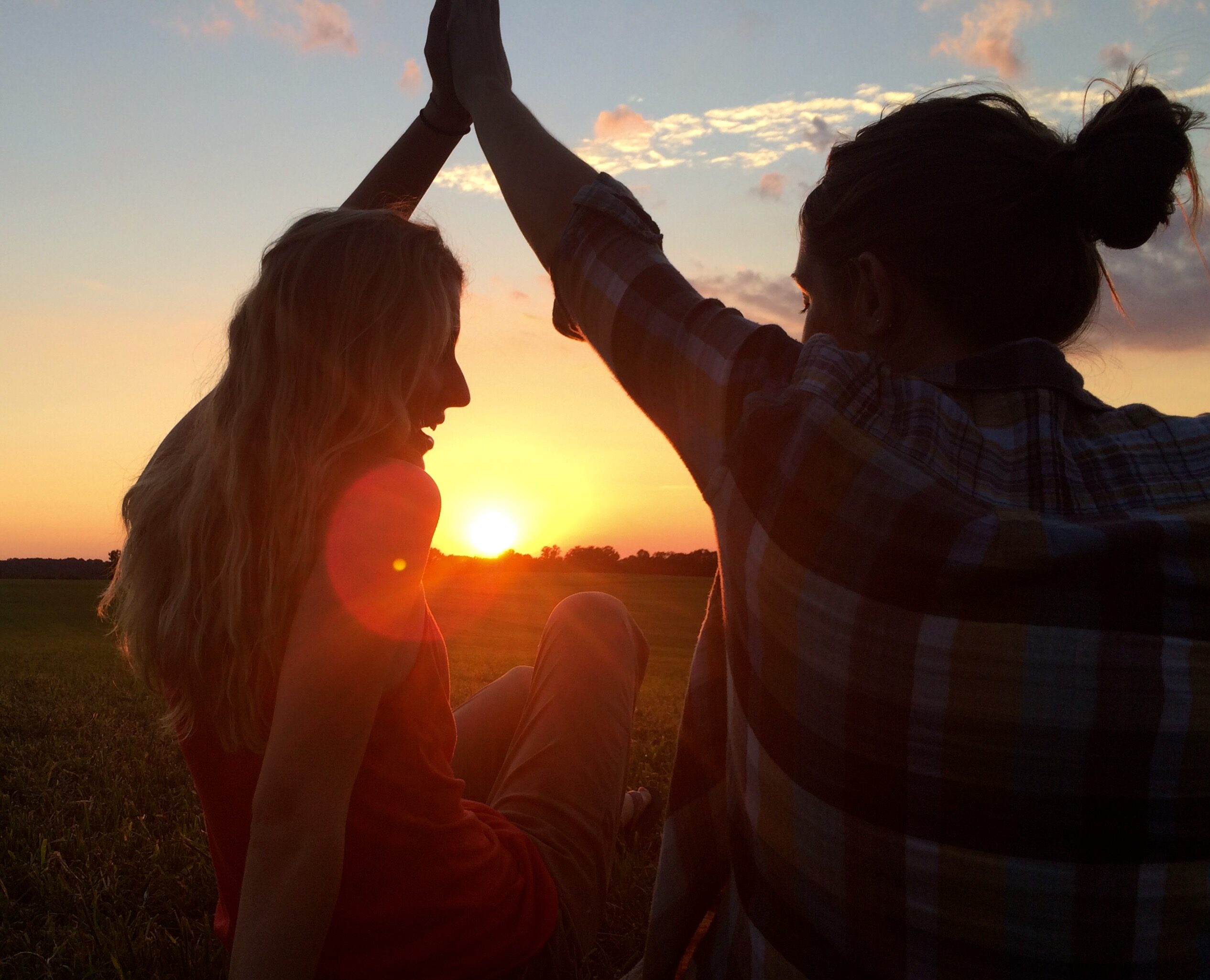 Two people high five in outdoors while the sun sets in the background.