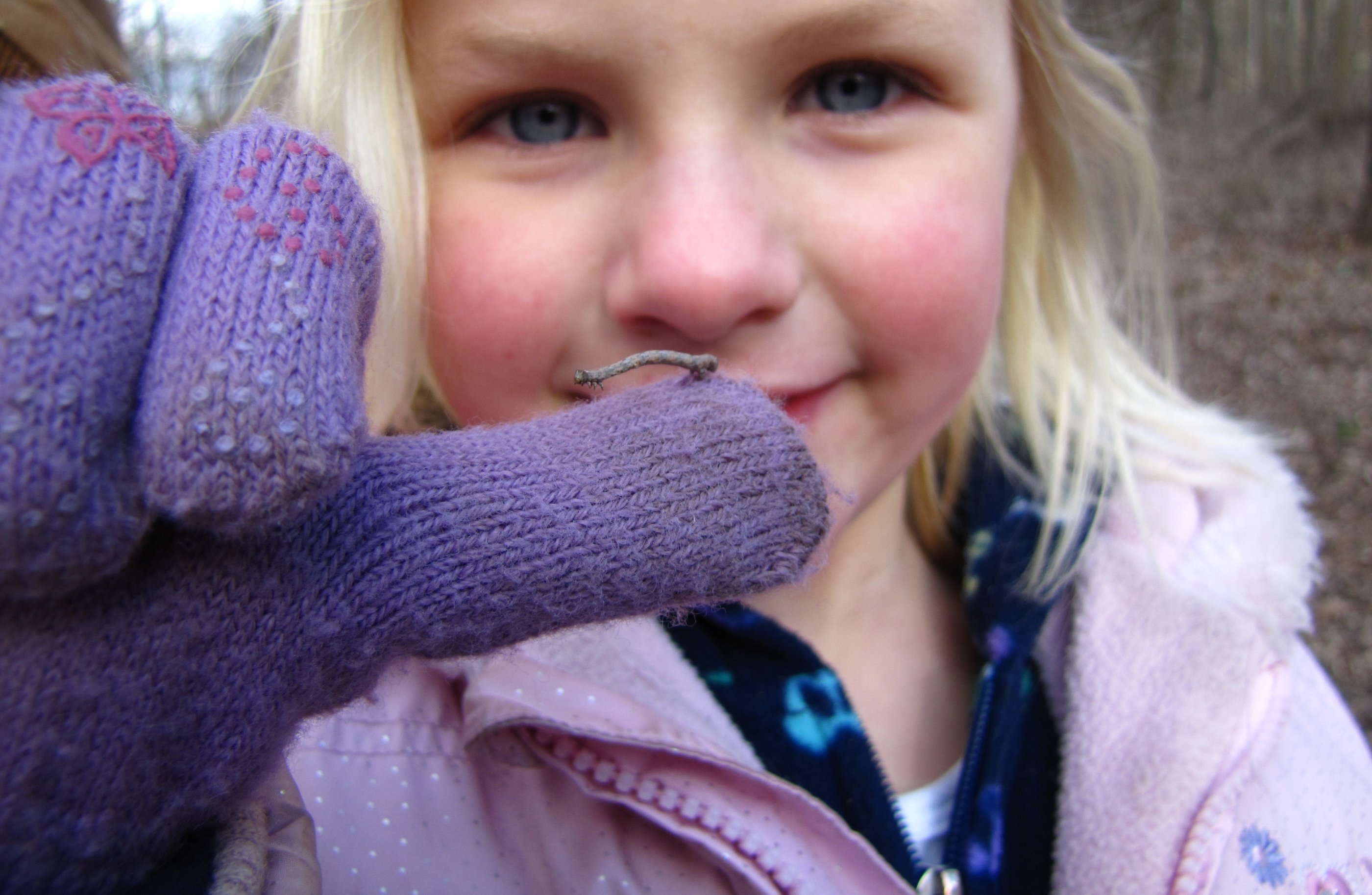 A child holds a small worm on a purple glove.