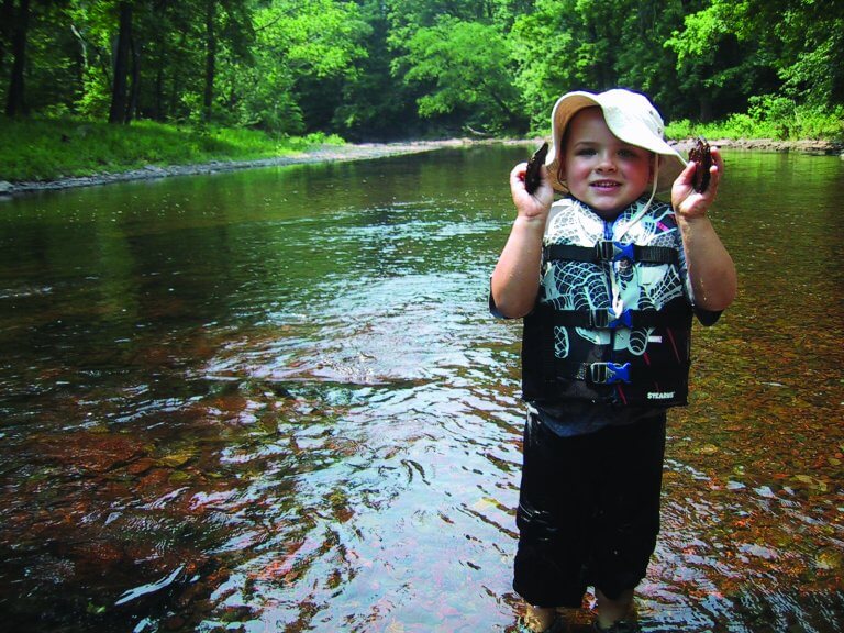A child smiles while standing in a stream.