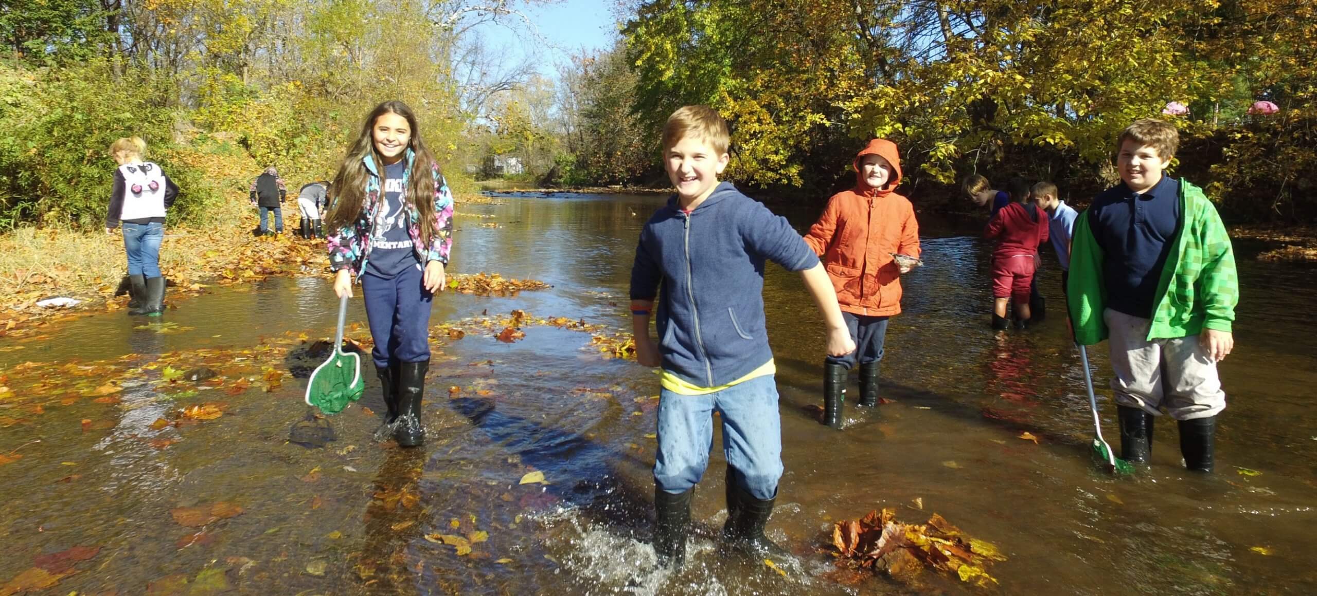 A group of children smile while playing in a creek.