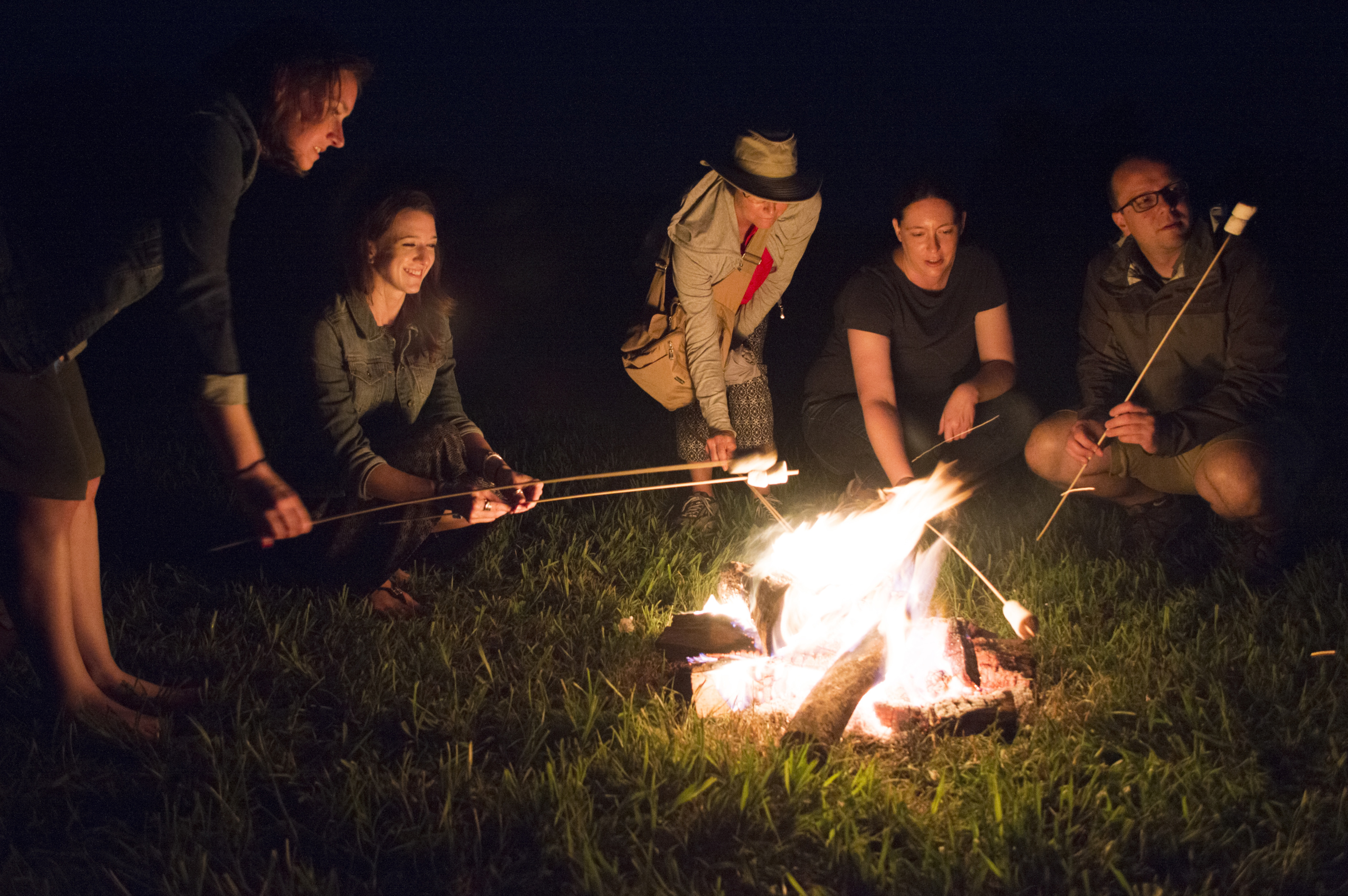 A groupd of people roast marshmellows on a fire outdoors at night