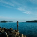 Photo of Caleb Arrowood standing outdoors on rocks next to the water.