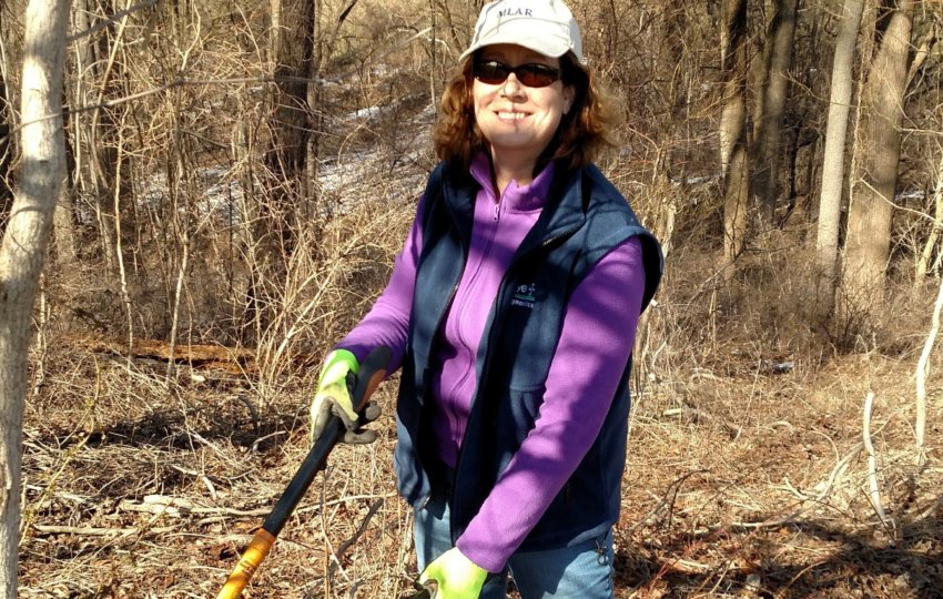 A volunteer smiles at the camera while holding hand tools.