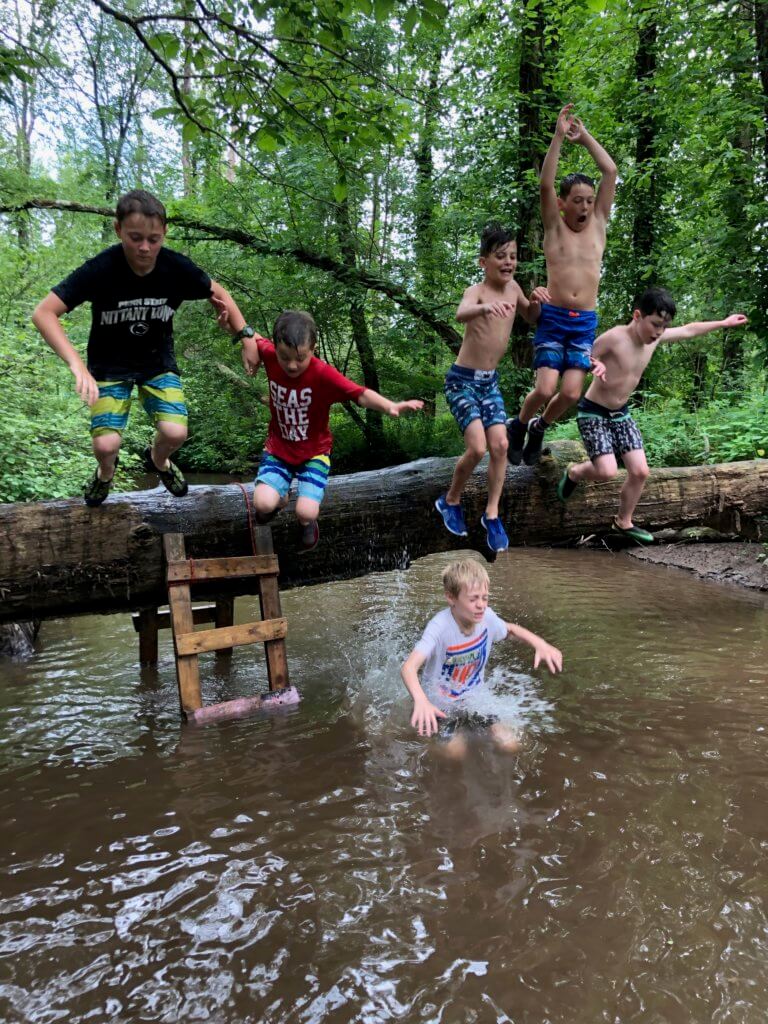 A group of children jump from a log into a stream.