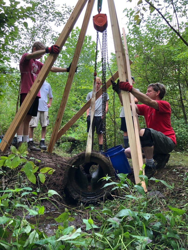 A group of people set up a wooden structure in a natural setting.