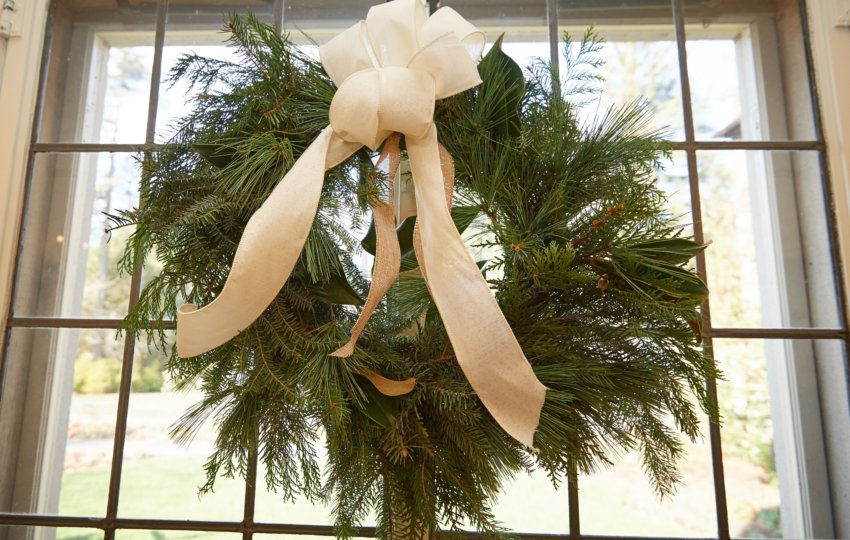 An evergreen wreath with a white bow hands on a window.