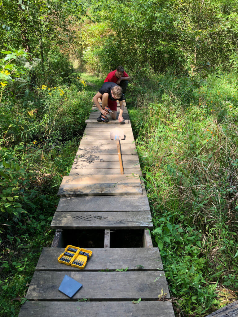 People work on a wooden boardwalk on a trail.