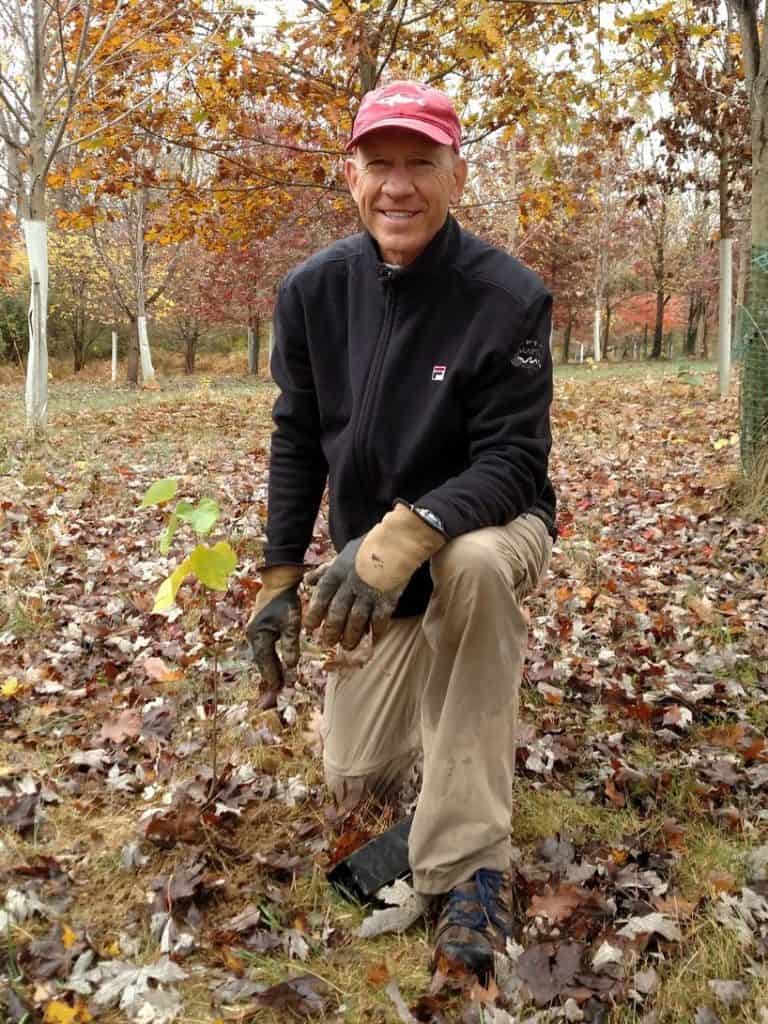 A man volunteer kneeling at newly-planted tree, smiling at the camera.