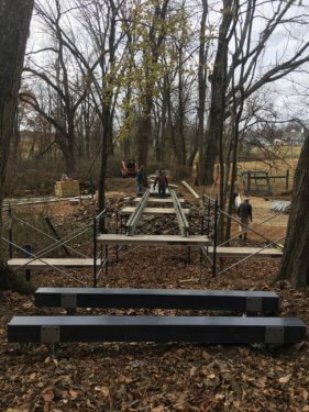 A wood and metal bridge under construction in a forest.