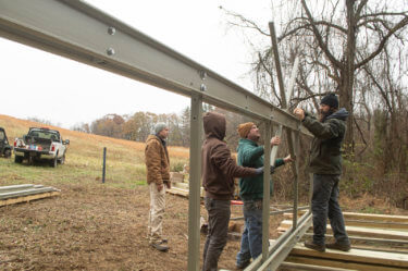 Four people in winter clothes work with hand tools on a metal structure.