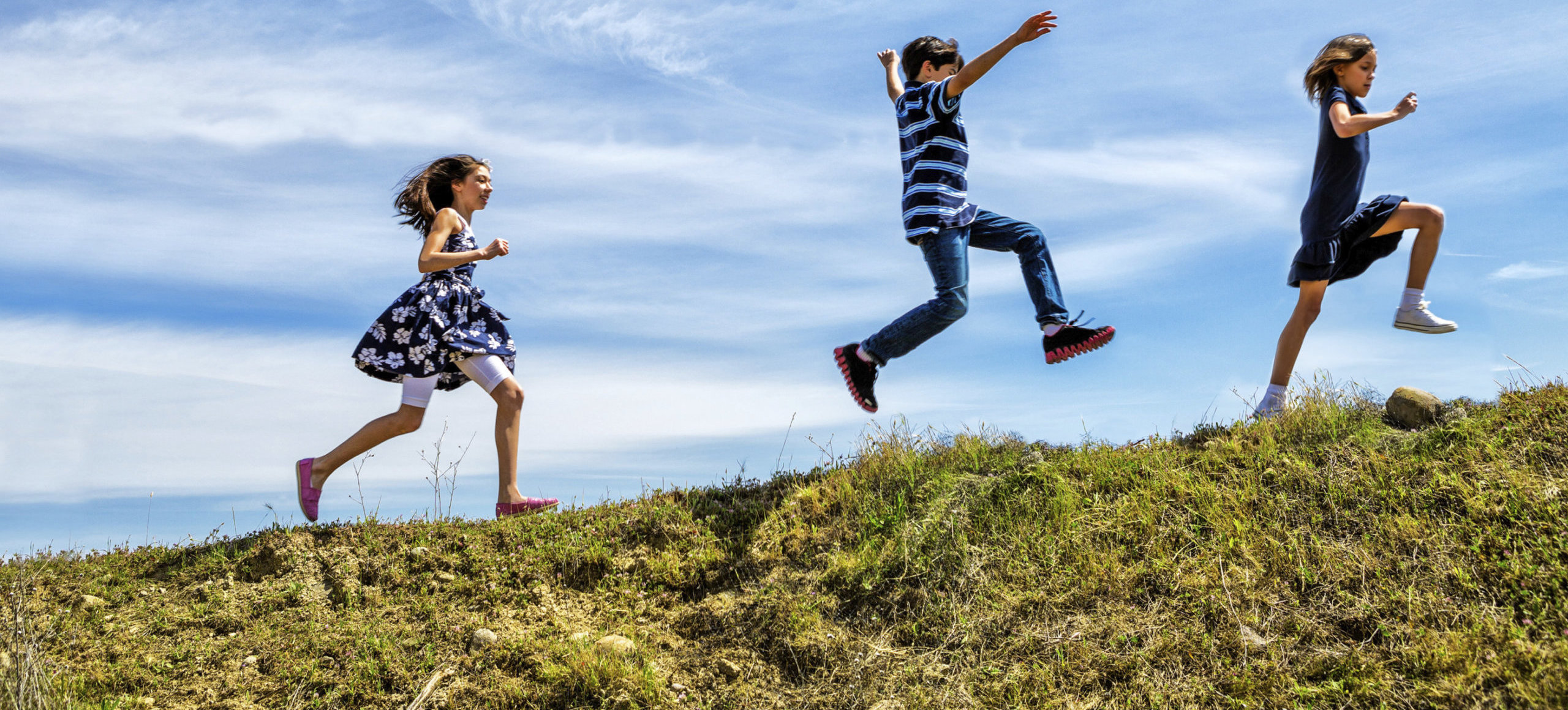 Three children run and jump across the grass.