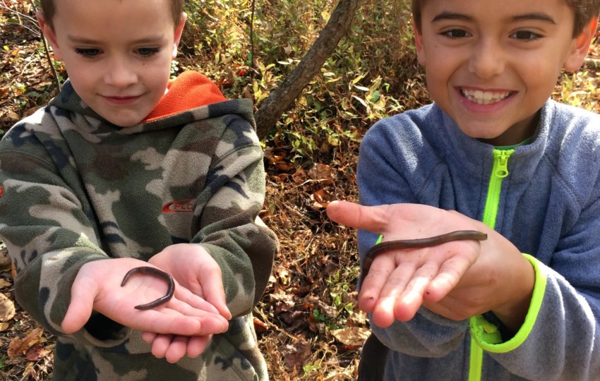 Two children smile while holding worms.