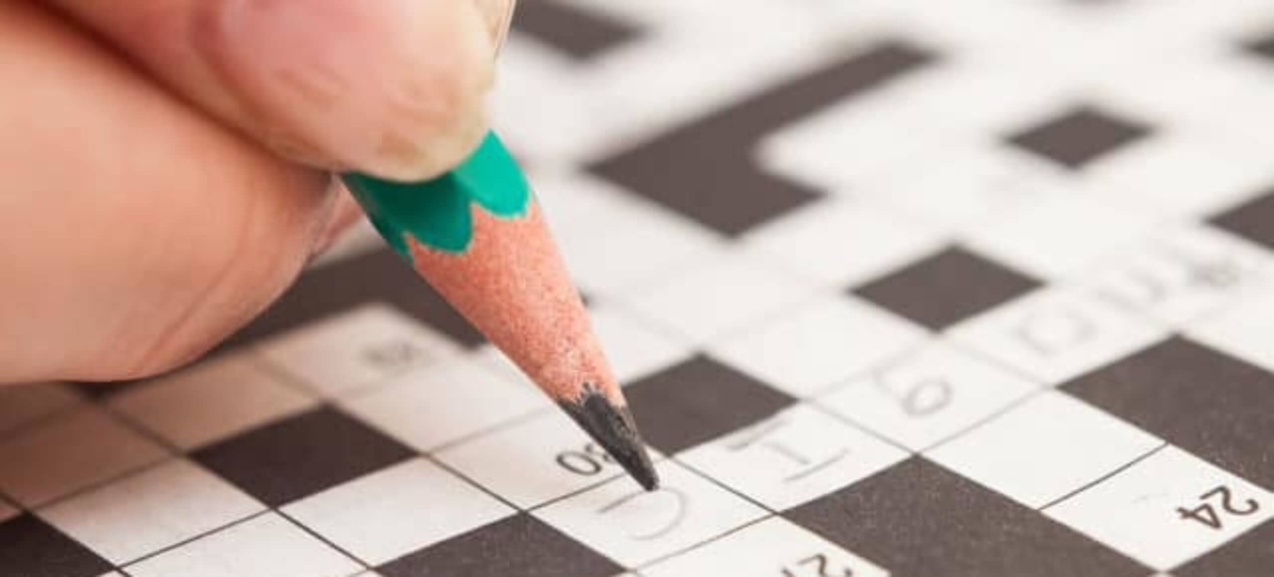 Close up of a hand holding a pencil over a crossword puzzle