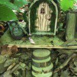 A fairy house of natural materials sits among brown leaves.
