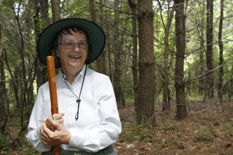 Headshot of Eileen Mc Donnell smiling while holding a walking stick outdoors.