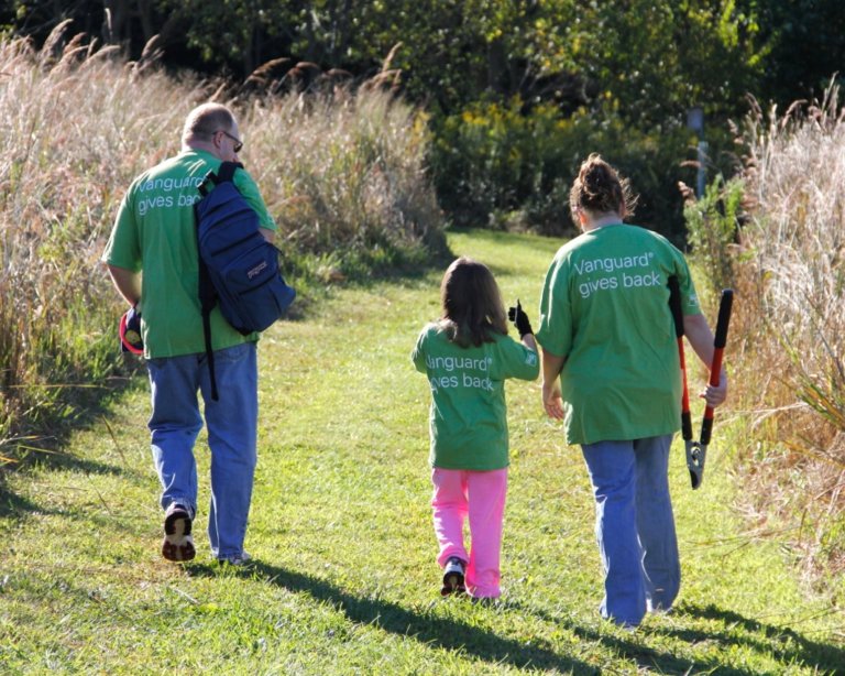 Three people walk along a grass trail holding hand tools.
