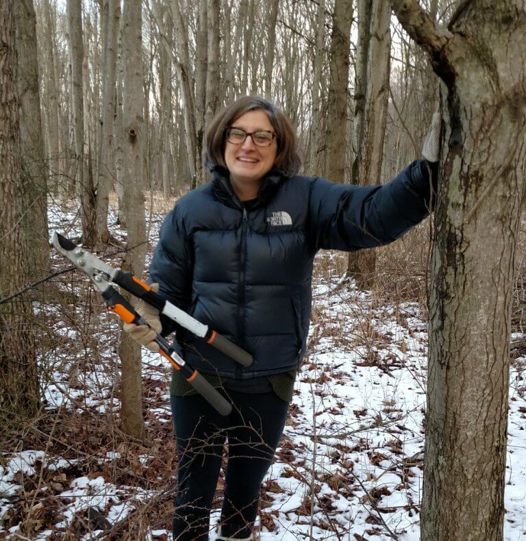A woman holds loppers in a winter forest.