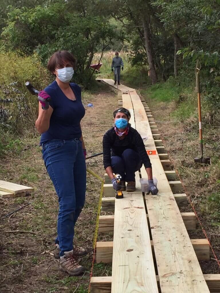 Two volunteers works with hand tools on a wooden boardwalk