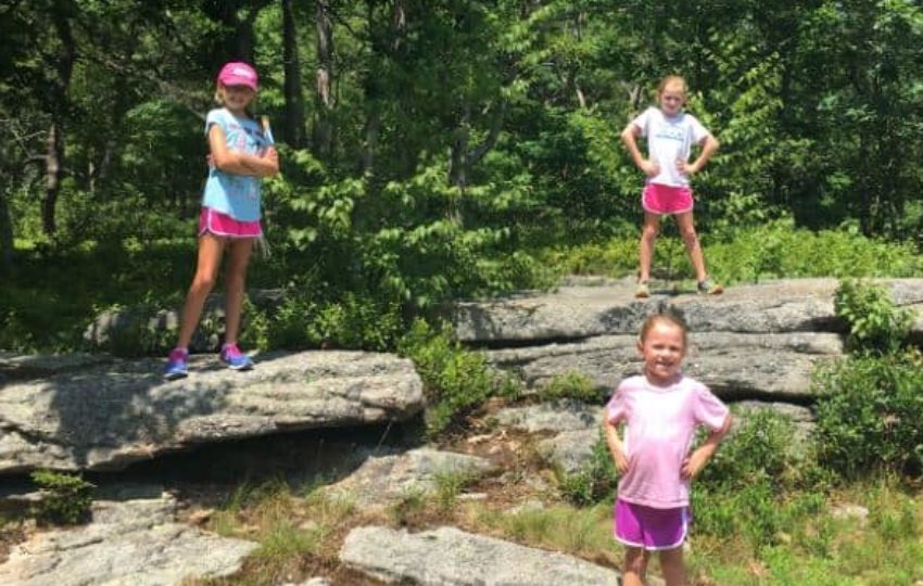 Three girls in shorts and tshirts posing for the camera on boulders in front of shrubs and trees