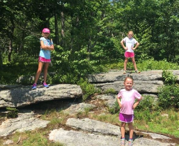 Three girls in shorts and tshirts posing for the camera on boulders in front of shrubs and trees