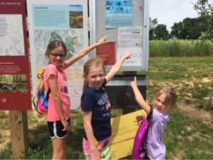 Three girls point at a map kiosk