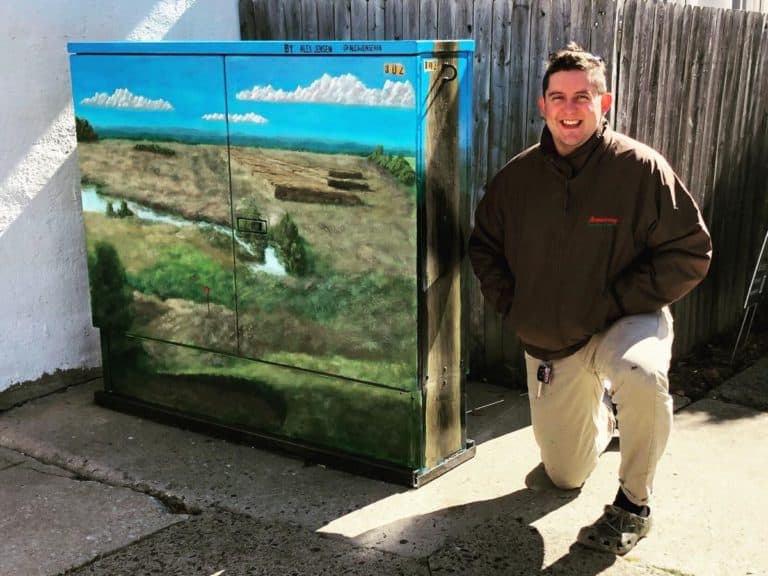A young man poses next to a mural he painted outdoors