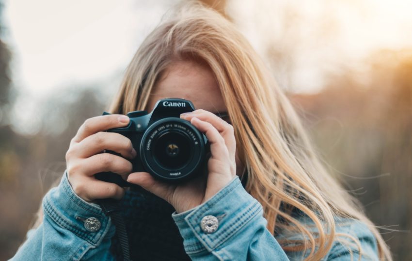 A woman in a jean jacket holds a camera in front of her face.