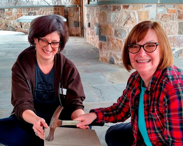Two female volunteers use a hammer to construct a bird box.