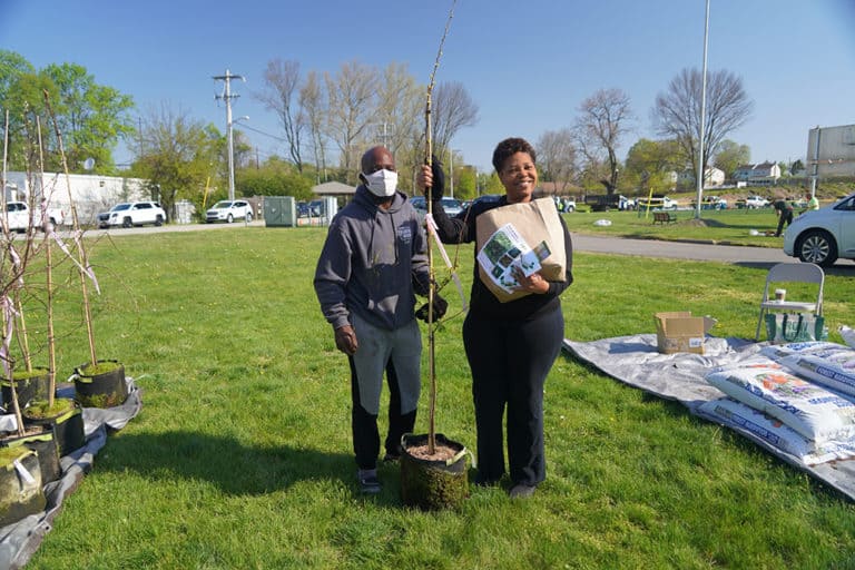 A man and woman posing next to a tree seedling