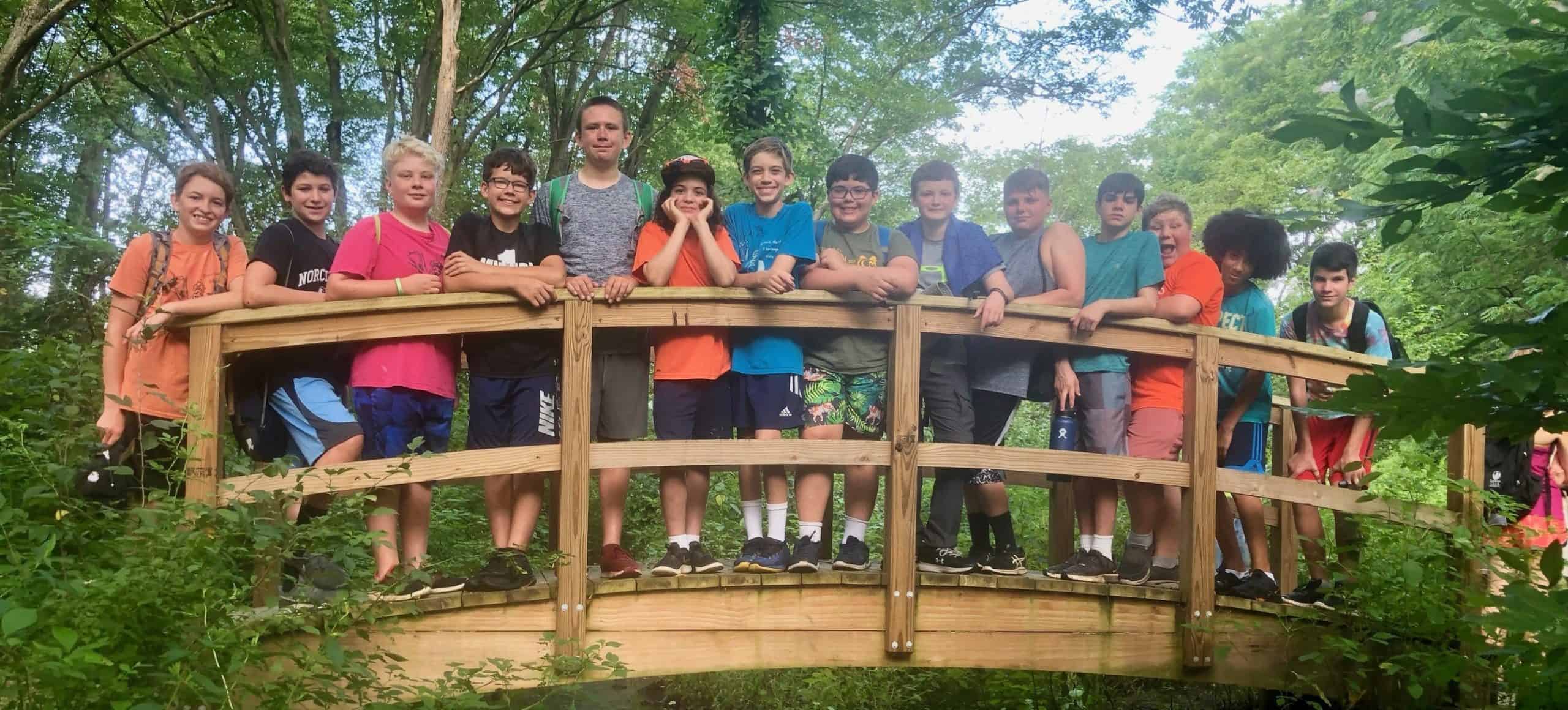 A group of youths standing on a wooden bridge over a woodland stream