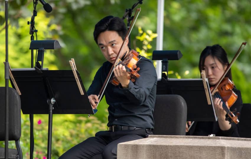 Several musicians playing violins outdoors
