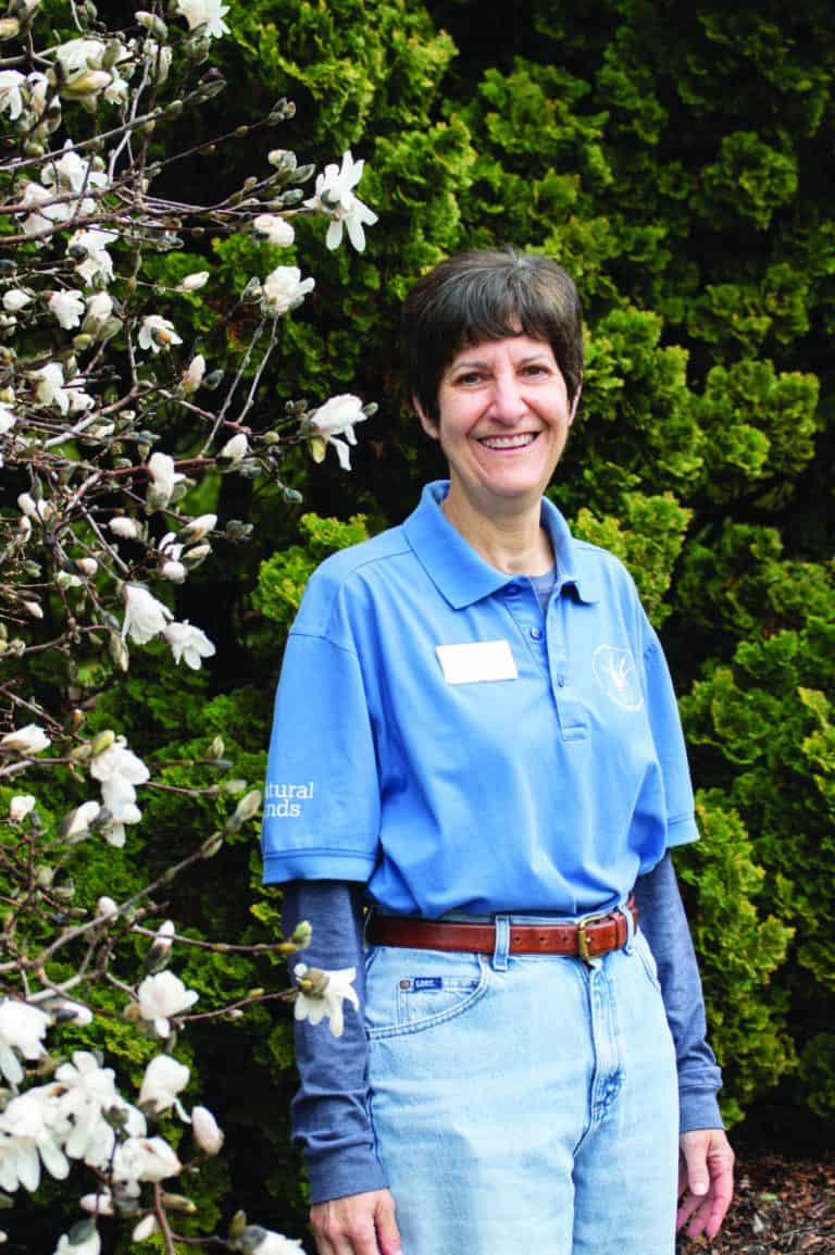 A woman with short brown hair stands smiling in front of a white blooming magnolia tree